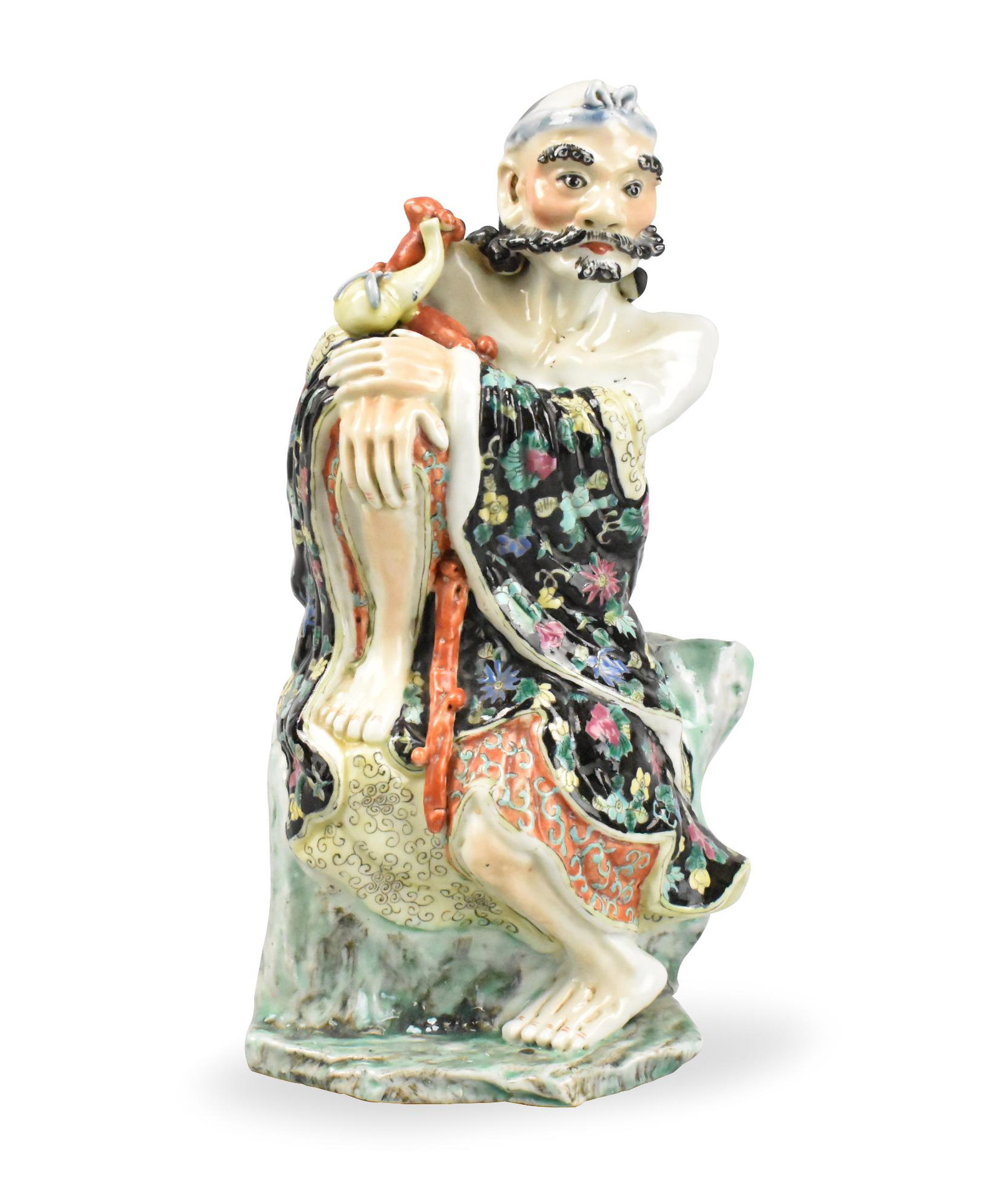 Chinese Famille Rose Figurine, ROC Period: A Chinese famille rose figurine, dating from the Repbulic period. A colorful male figure with draping robe festooned with flowers perches on a rock outcropping with one knee up, both hands resting on 