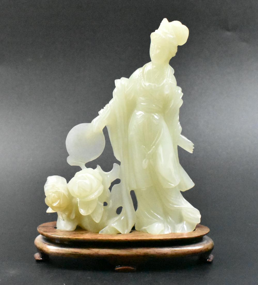 Chinese Jade Carved Lady Figure on Stand: A Chinese jade carved lady figure on wooden stand. The lady figure stands in her flowing robes holding a fan in her right arm, beneath which is two large flowers in bloom. Accompanied by a custom oval