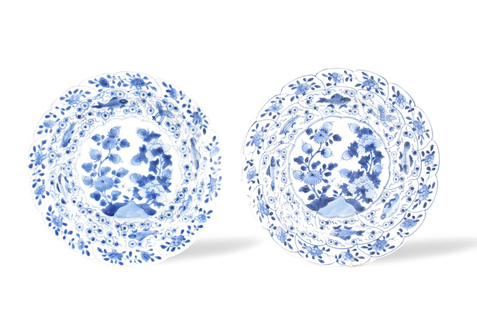 Pair of Chinese B & W Floral Plates, Kangxi Period: A pair of Chinese blue and white floral plates, dating from the Kangxi period (1661-1722). Each plate features a dense design of flowers and fish. Central design of flowers in bloom, surrounded by a r