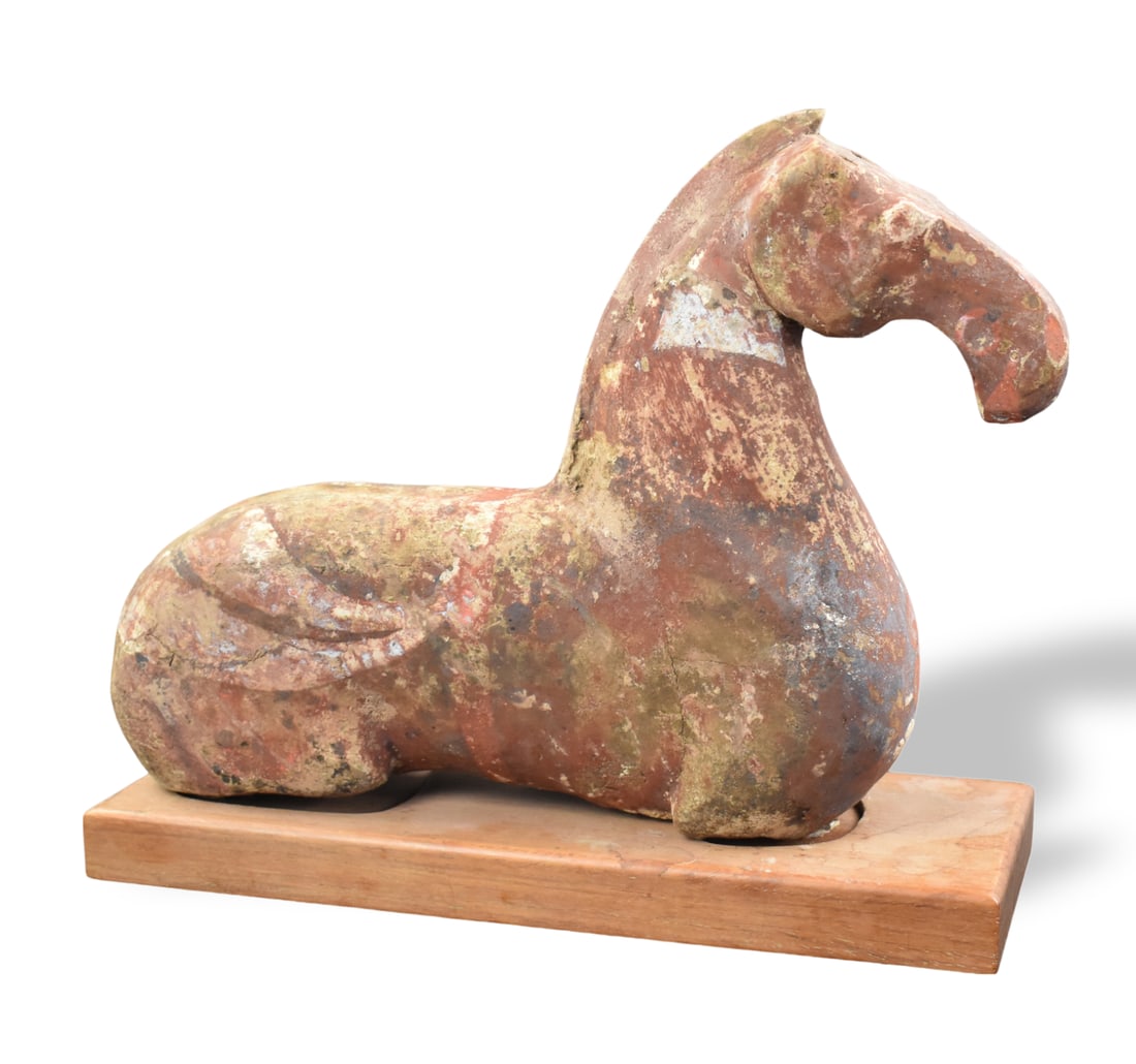Chinese Pottery Recumbent Horse, Han Dynasty: A Chinese pottery recumbent horse on wooden rectangular base, dating from the Han dynasty. molded with an elongated sway back and rounded hindquarter, Painted at one time with remnants of paint on the