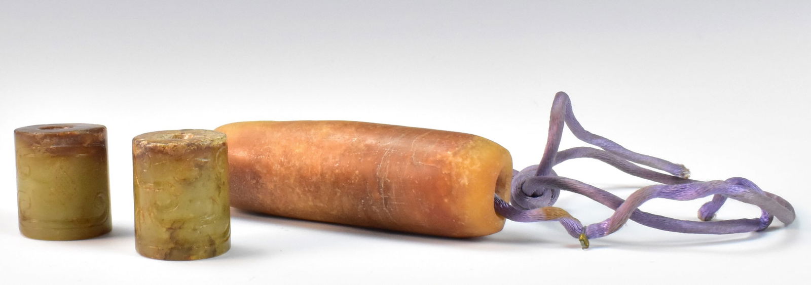 3 Chinese Archaic Jade Beads: Three archaic Chinese jade beads, two cylindrical celadon jade beads and a long, brownish red bead. The two celadon beads have flat sides and incised archaic design around body. Longer bead has swirl