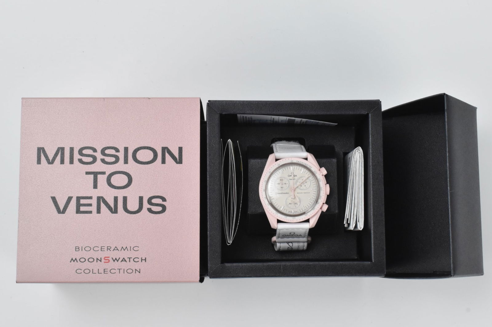 MoonSwatch Mission to Venus Omega Bioceramic Col: A Moonswatch Mission to Venue Omega Swatch. From the Bioceramic MoonSwatch Collection. With white face in pink frame and white velcro strap. Paperwork Aug. 16, 2024. Link to HD Natural Light photos:
