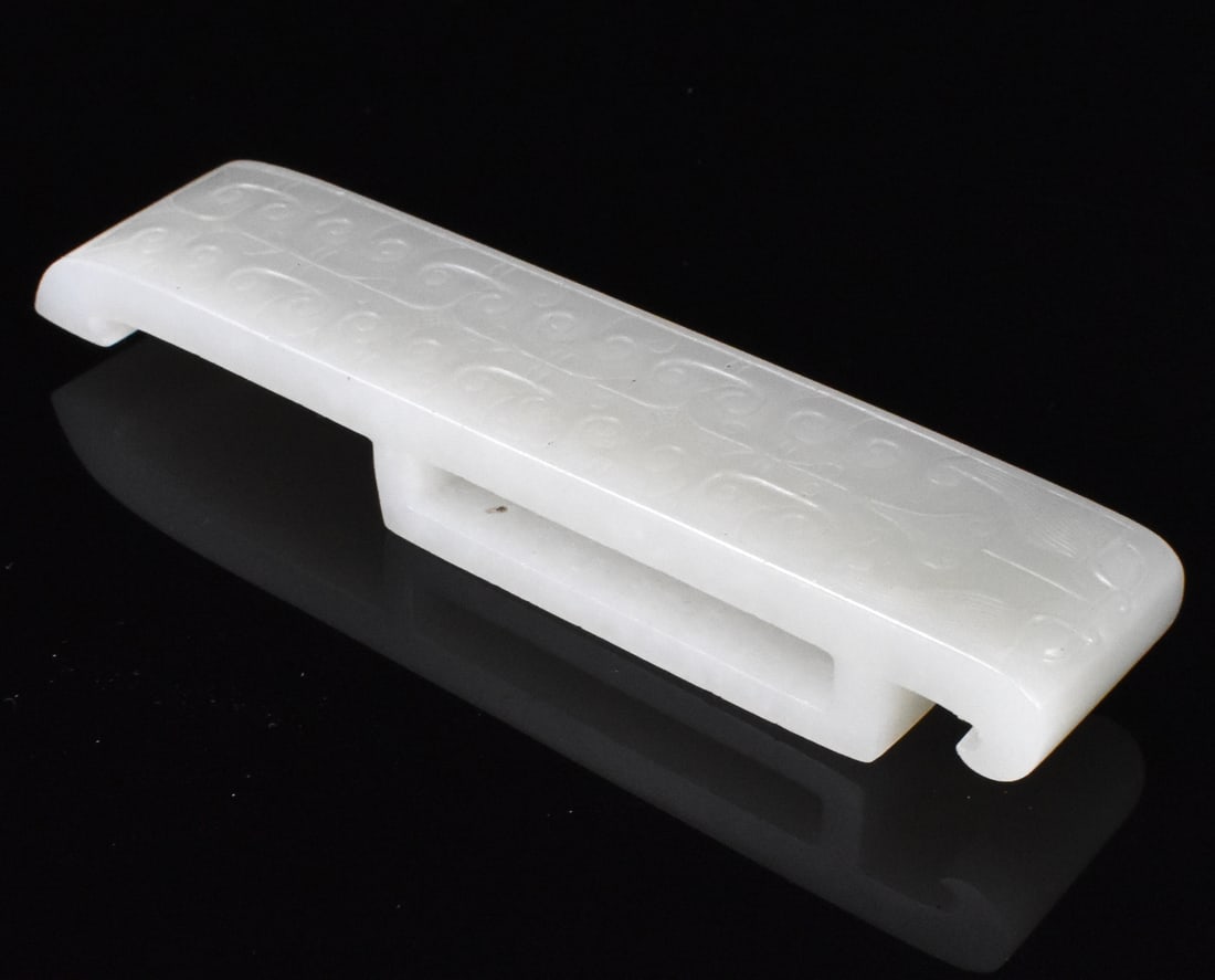 Chinese White Jade Carved Sword Guard, 19th C.: A Chinese white jade carved sword guard, dating from the 19th century. The long rectangular shape has lightly incised Taotie image at one side with symmetrical archaic scrolls along the length. L. 4 3