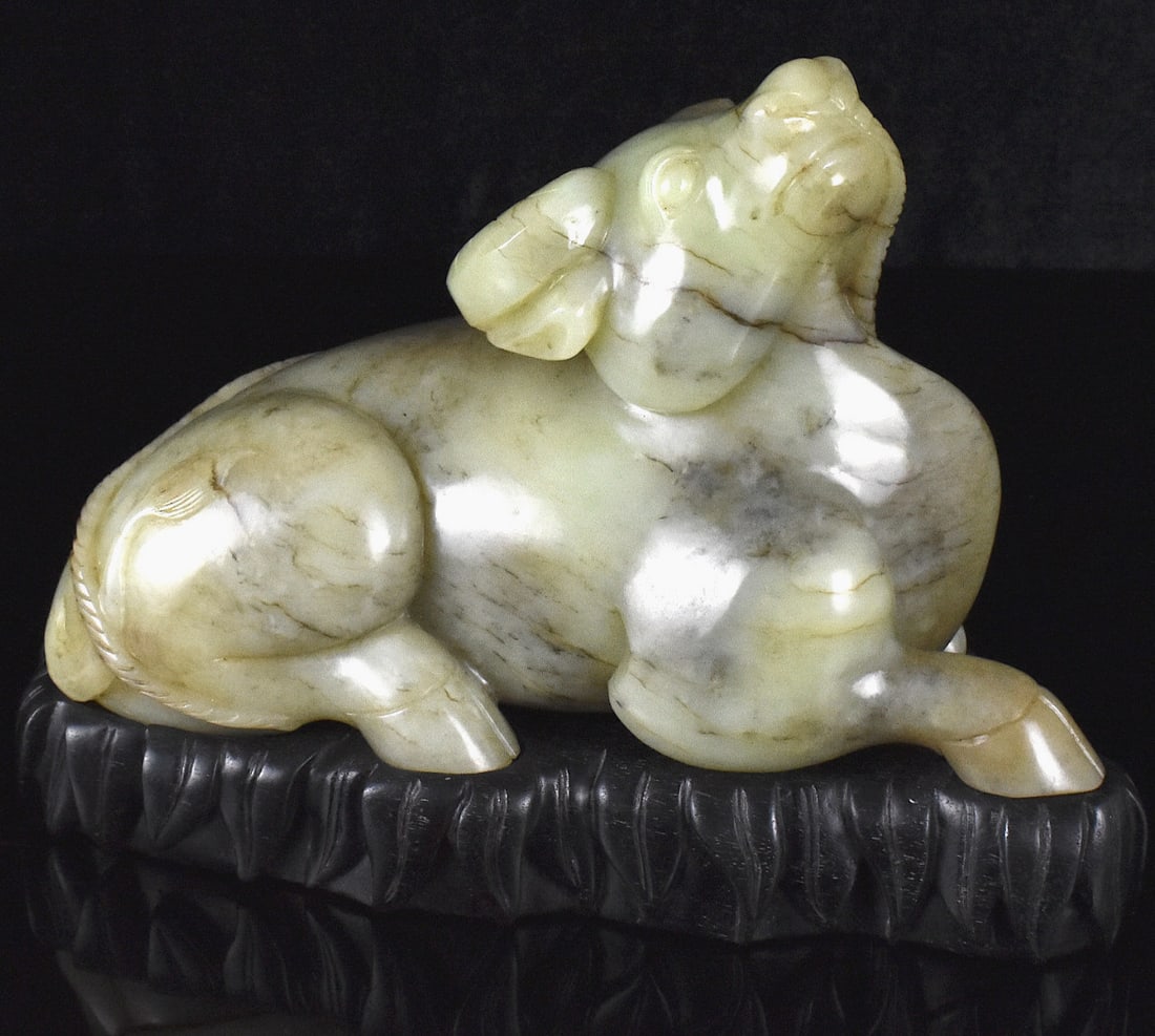 Large Chinese Jade Carved Buffalo on Stand: A large Chinese jade carved buffalo on wooden stand. Carved from single block of jade the animated buffalo, seated, rears its head up with a rope tied to its nose, wrapping around its body. Detailed h