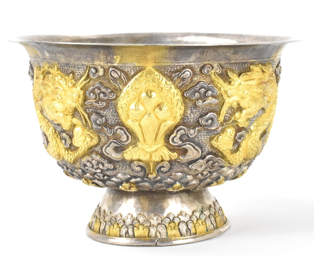 Tibetan Gilt Silver Stem Dragon Bowl,Qing Dynasty: A Tibetan gilt silver stem dragon bowl dating from the Qing dynasty. Two large repousse gilt dragons raised on the exterior of the deep stem bowl, amongst clouds and over waves. on a splayed tall foot