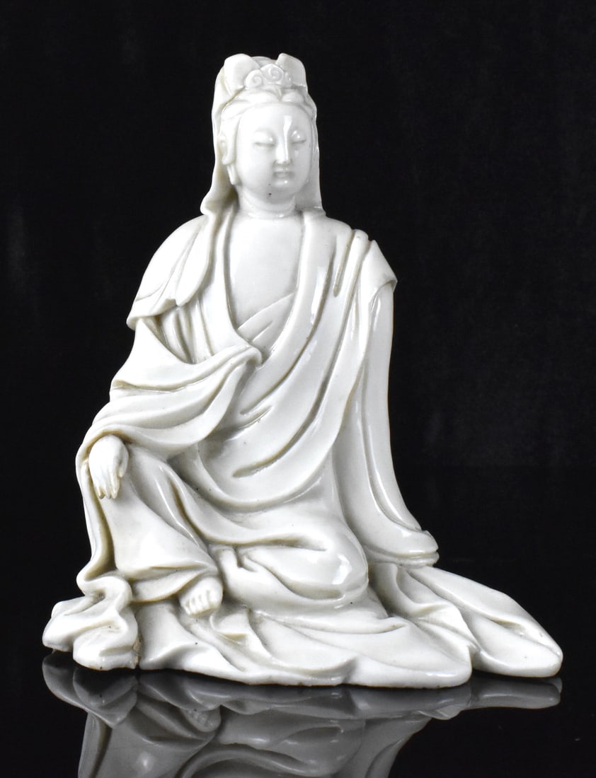 Chinese Blanc De Chine Guanyin Figure, 19th C.: A Blanc de Chine Guanyin figure, dating from the 19th century. The Guanyin is at ease, seated on ground covered with her robe, leaning on left hand, with right hand resting on bended knee. Her eyes ar