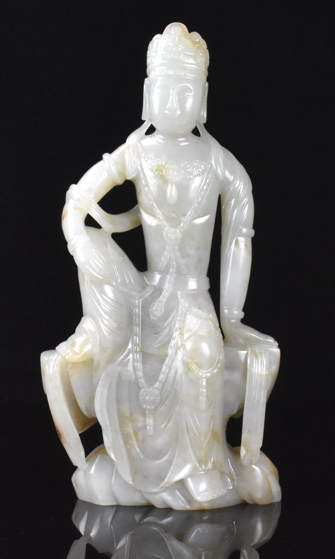 Chinese Jade Carved Seated Guanyin ,Qing Dynasty: A Chinese jade carved seated Guanyin figure, dating from the Qing dynasty. The Guanyin sits upright on a rocky form with right knee up and right arm resting on it. Guanyin is adorned with arm bands an