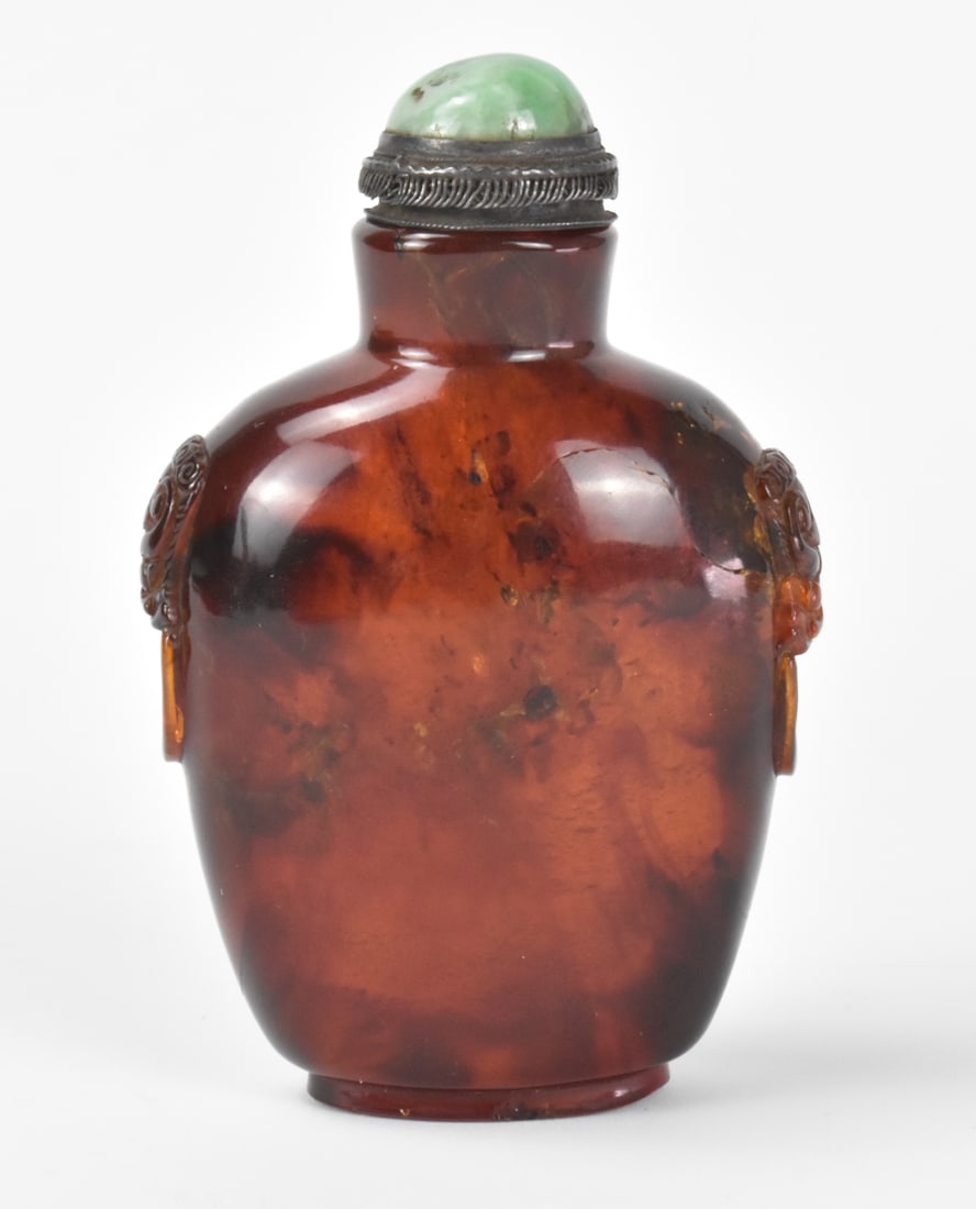Chinese Amber Carved Snuff Bottle, Qing Dynasty: A Chinese amber carved snuff bottle, dating from the Qing dynasty. A large bottle of oval form with wide shoulders tapering to a straight, short neck. An intact metal spoon with jadeite set in the top
