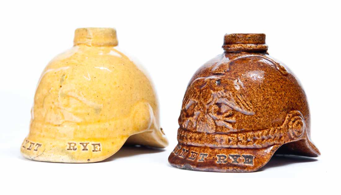 TWO FIGURAL "HELMET RYE" FLASKS: American, 19th century. German-type helmets with eagles on the front. Includes a yellow ware flask marked for Max Fruhauf & Co., Cincinnati, Ohio, the other with with a brown glaze and without a retai