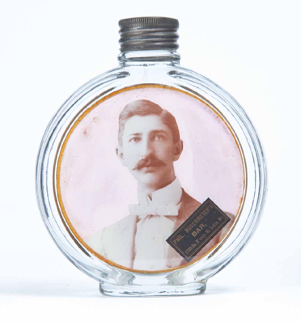 ST LOUIS, MISSOURI GLASS FLASK: Pressed-glass flask with attached photographic panel for "PHIL. ROSENMEYER'S BAR, 1730 So. B'way, St. Louis, Mo." Retains its tin cap. 5" high.