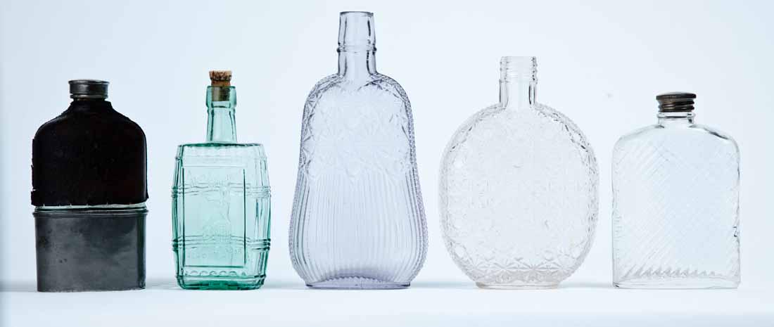 GROUP OF FIVE FLASKS: Late 19th-early 20th century, pressed glass. Three colorless flasks with geometric patterns, 5.75" to 7.75" high; one aqua flask with a dancing girl and "Merry Christmas AND A Happy New Year," 5.5" hi