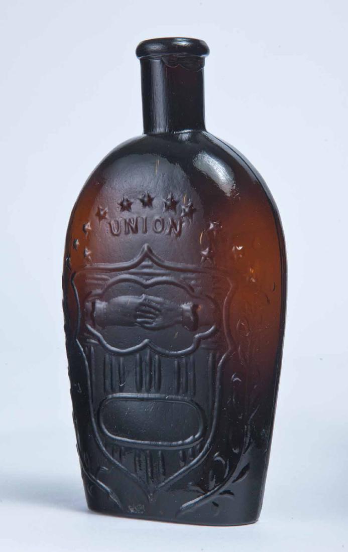 EAGLE & CLASPED HANDS FLASK: GXII-33, Midwestern, mid-19th century, half pint, dark amber in color, with clasped hands and "UNION" on the obverse and an eagle over a blank frame on the reverse, rounded lip and plain bottom. 6.25"
