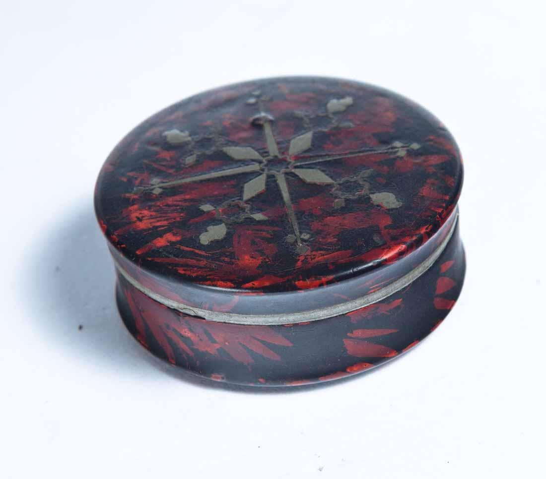 LACQUERWARE SNUFF BOX: Round with red and black paint decoration and inlaid silver geometric accents. Purchased from Hollyhock House Antiques, Bucyrus, Ohio. .75"h. 1.75"dia.