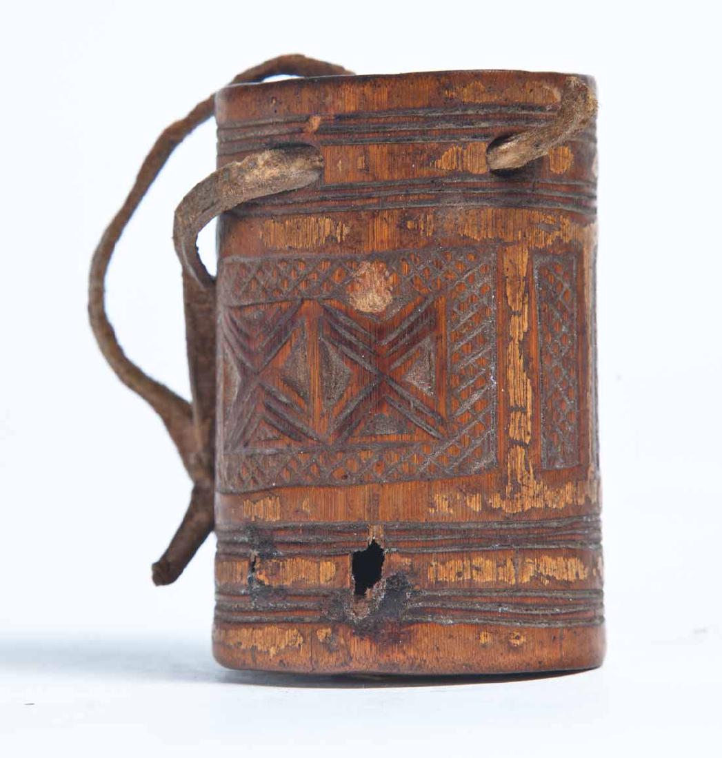 CHIP CARVED WOOD BARREL SNUFF BOX: Round with geometric and line decoration around the exterior. Round plug attached with knotted leather thong for lid. 2.5"h. 1.75"dia.