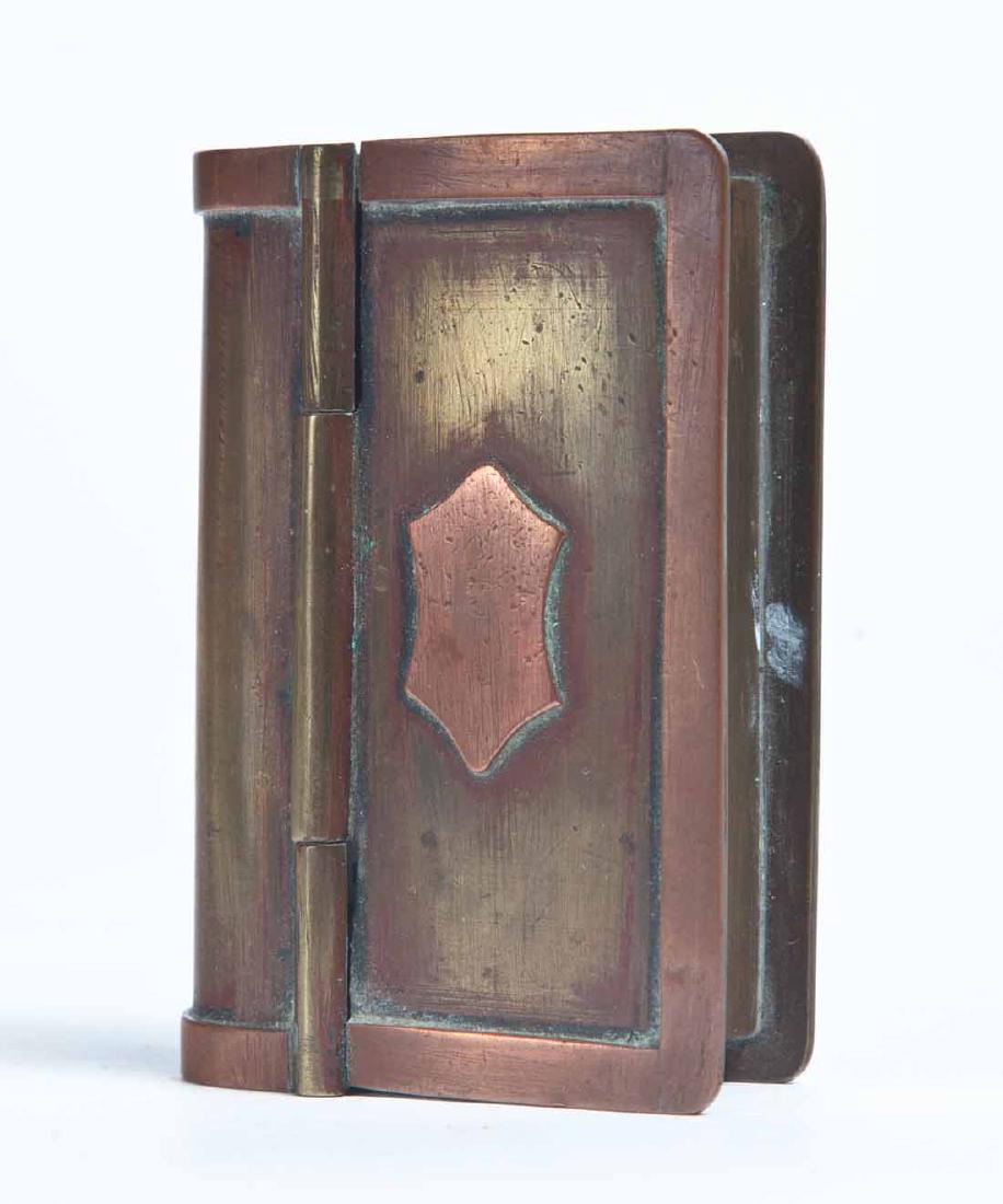 BOOK-SHAPED SNUFF BOX: Copper and brass with hinged lid and embossed medallion in center. .75"h. 3"w. 2"d.
