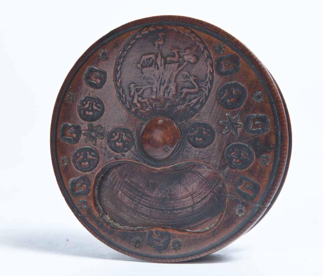 WOOD WITH EMBOSSED DECORATION AND ROTATING LID: Round with an hourglass-shaped opening and embossed decoration of a hunter and deer and flowers. 7/8"h. 3.25"dia.