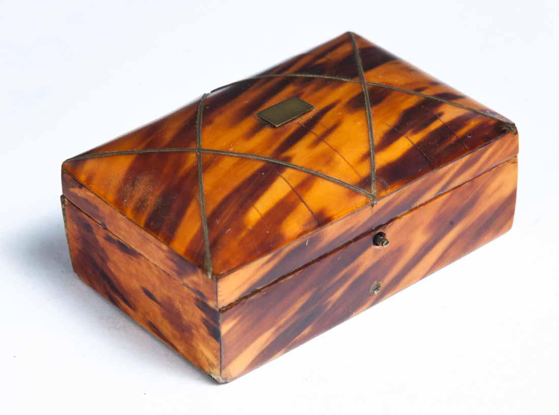 DOME TOP SNUFF BOX: Rectangular with single hinge lid crossed by inlaid brass bands and central blank name tag. Tortoise shell veneer on exterior, silk lined lid and white paper with blue flowers lining the inside base. 