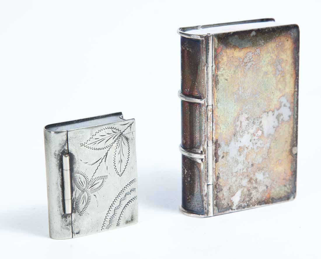 TWO BOOK-SHAPED SNUFF BOXES: Both silver plate. Larger with well-defined spine bands. .5"h. 2 .5"w. 1 .75"d. Smaller with etched flower and scalloped arcs on lid. .5"h. 1.5"w. 1"d.