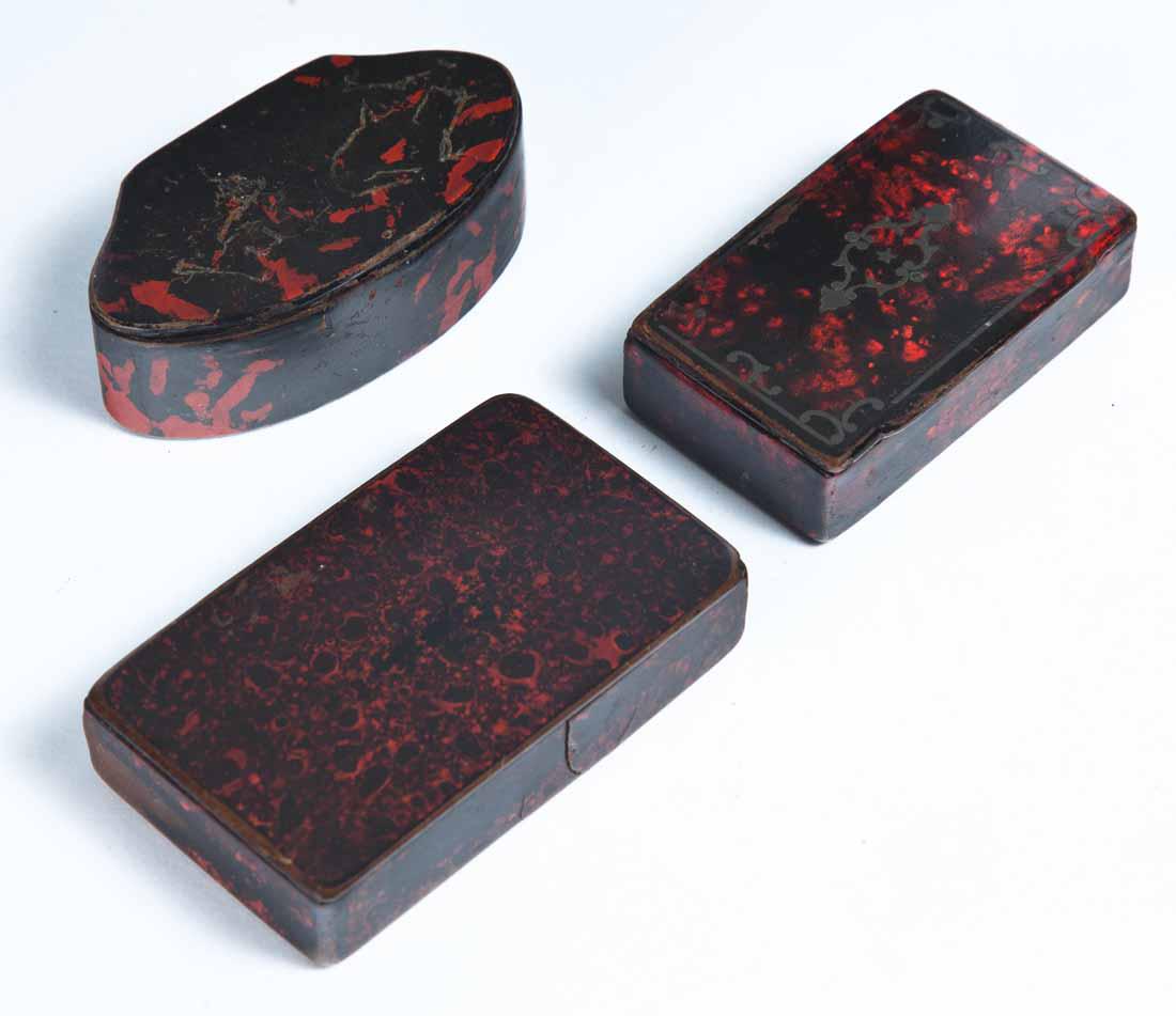 THREE LACQUERWARE SNUFF BOXES: All with black and red marbled paint. Two rectangular, one with metal inlay on lid. 2"w. 3.5"w. One oval with shaped side. 3.25"w.