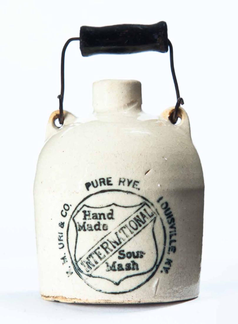 LOUISVILLE, KENTUCKY MINIATURE ADVERTISING JUG: Cream glaze and bail handle, and with stamped advertisement "INTERNATIONAL Hand Made Sour Mash PURE RYE K.M. URI & COâ€¦" 3" high excluding handle.