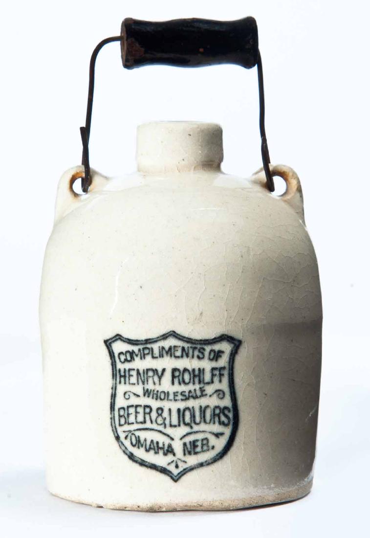 OMAHA, NEBRASKA MINIATURE ADVERTISING JUG: Cream glaze, bail handle, and stamped advertisement "COMPLEMENTS OF HENRY ROHLFF WHOLESALE BEER & LIQUORSâ€¦" 3.25" high.