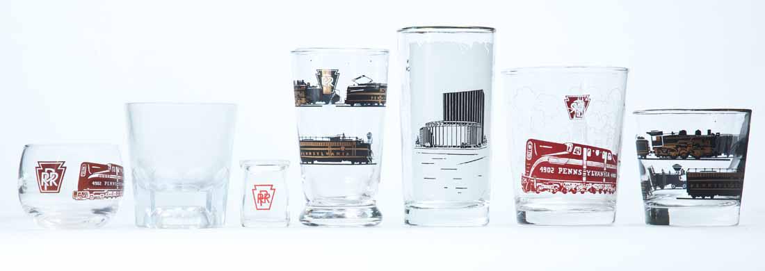 SEVEN PIECES PENNSYLVANIA RAILROAD GLASS: Lot includes an individual cream bottle from the Anchor Hocking Glass Company, five (5) drinking glasses with either black and gold or red and white decoration and one clear glass with "PRR" embossed
