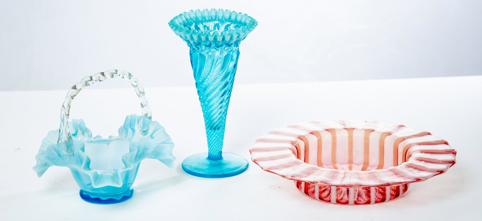 THREE PIECES OF VICTORIAN GLASS: American, late 19th century. Group includes blue trumpet vase with ruffled rim, cranberry basket and opalescent center bowl with wide flat rim. 1.75" to 7" high. (LR95)