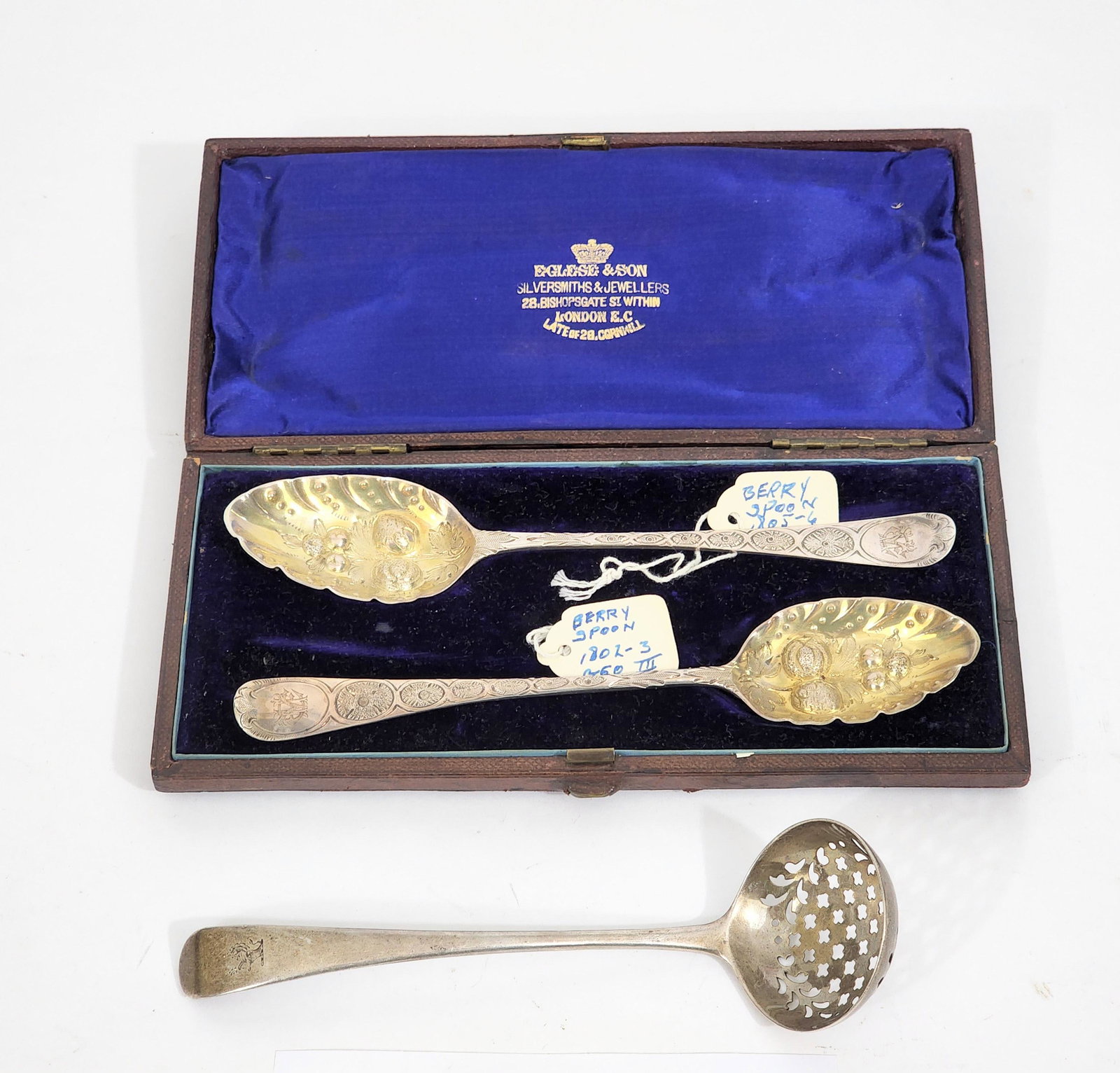 THREE GEORGIAN STERLING SILVER SPOONS: English, 18th century.Monogrammed "EM" pair of berry spoons with repousse flowers and chasing by Thomas Wallis II of London hallmarked "G" 1802 and "K" 1805 in a fitted case for Eglese & Son silversmi