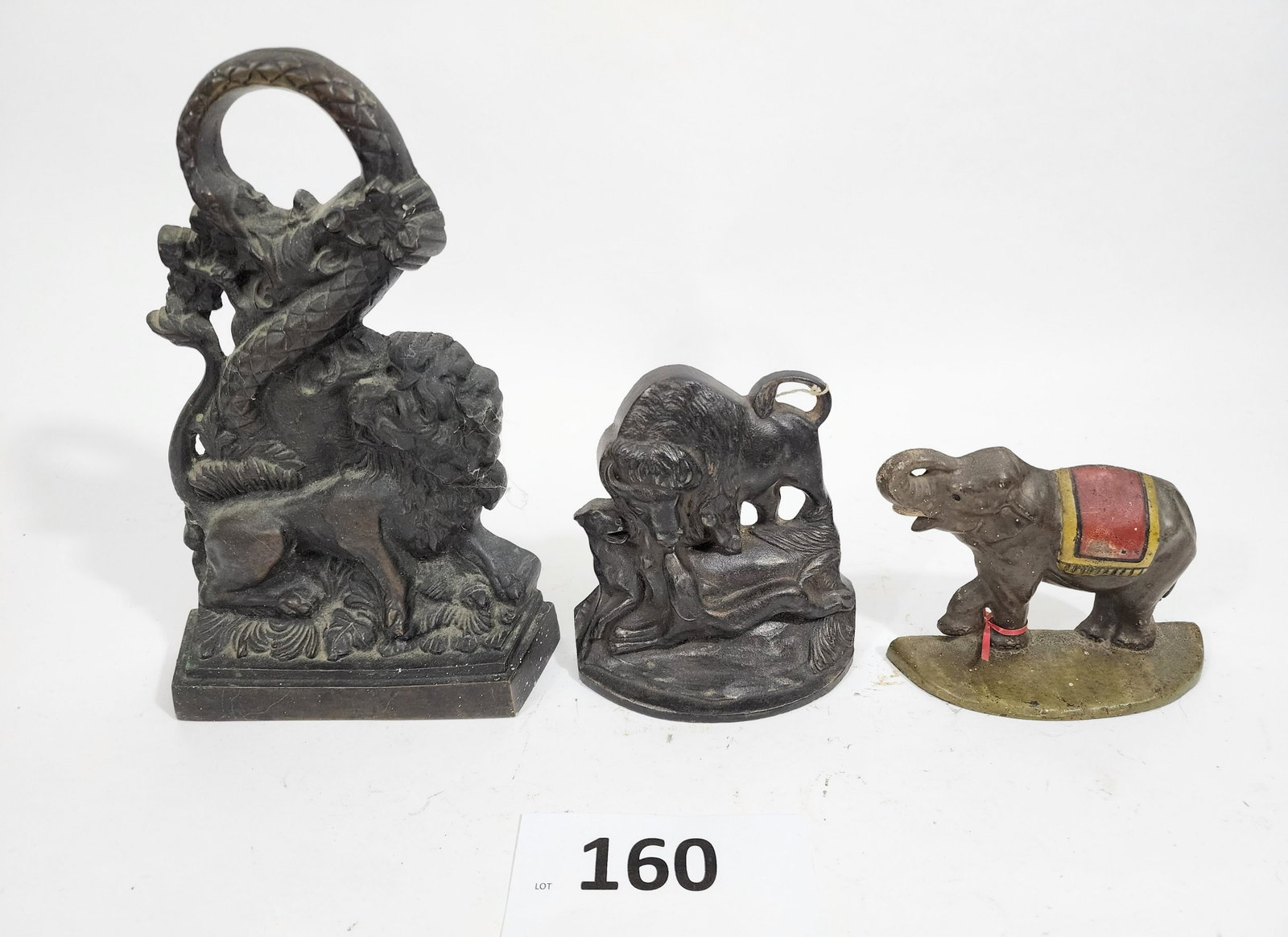 THREE DOORSTOPS: Early 20th century. Includes a brass lion and serpent, cast iron elephant and "Buffalo Hunt," 4.5" high to 10.75" high.