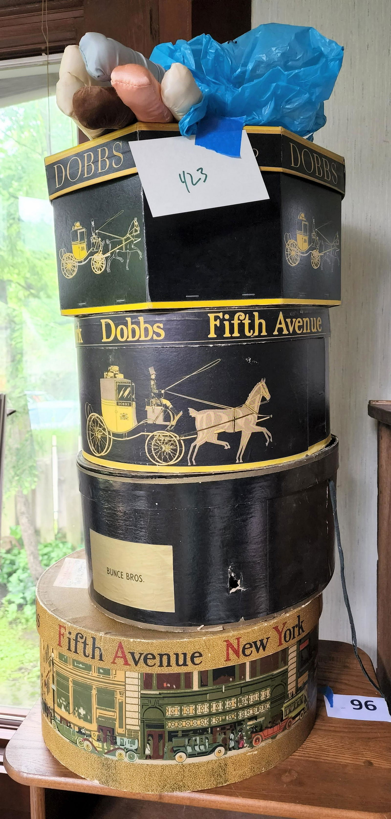 HAT BOXES, HAT, and CLOTH HANGERS: American, 20th century. Hat boxes and cloth hangers. From top to bottom, a selection of satin hangers, black Dobbs of New York hat box (2), a black Bunce Brothers hat box with hat included, and a poly