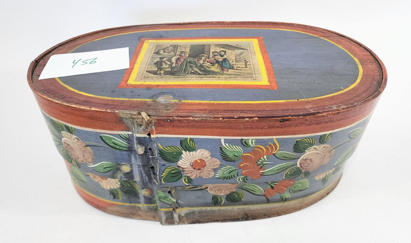 BRIDE'S BOX: European, 19th century. Oval bentwood box with original floral decoration on a blue and salmon ground, and with a decoupaged print of a fishing family on the lid. 17" long.
