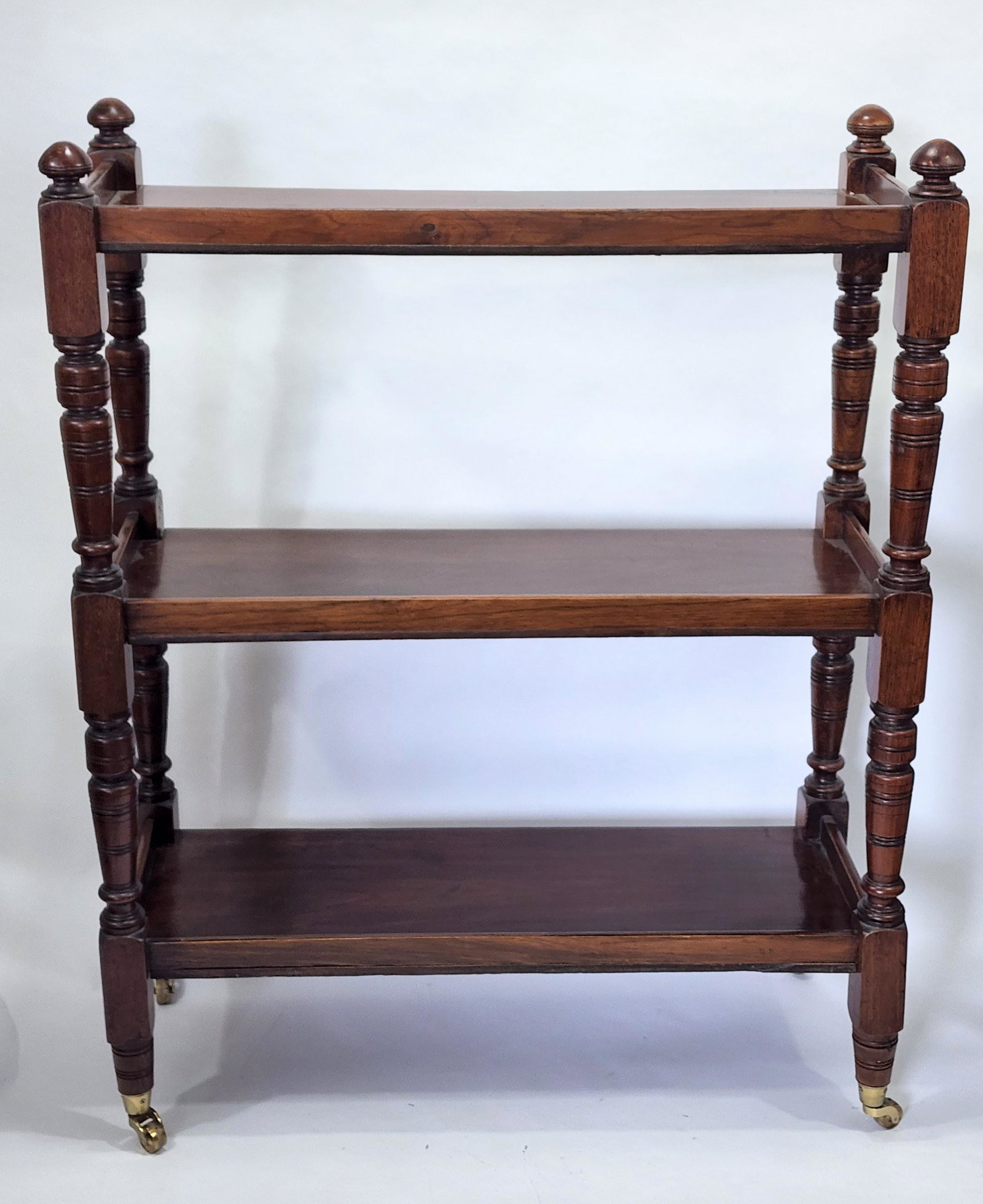 ENGLISH DUMBWAITER: Mahogany, 19th century. Three shelves on turned supports and with brass casters. 43.5" high, 34" wide, 14" deep.