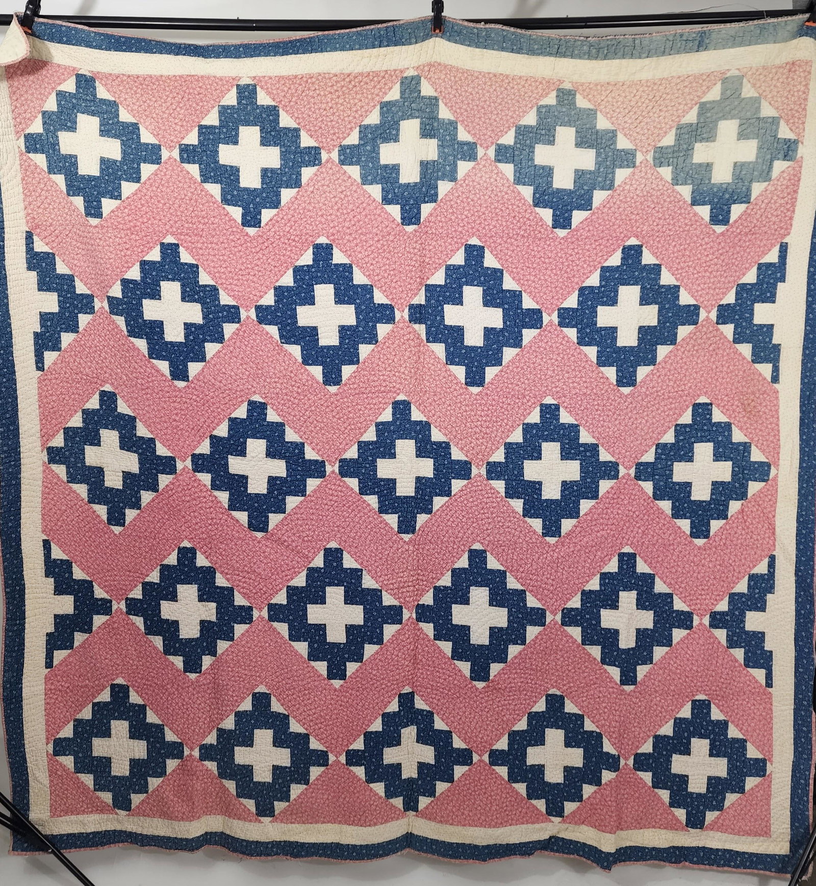 AMERICAN PIECED QUILT: Early 20th century. Pieced Album quilt with blue print and white solid album blocks on point separated by a double pink print pieced vertical zigzag. Same blue print forms outer border; pink binding. 