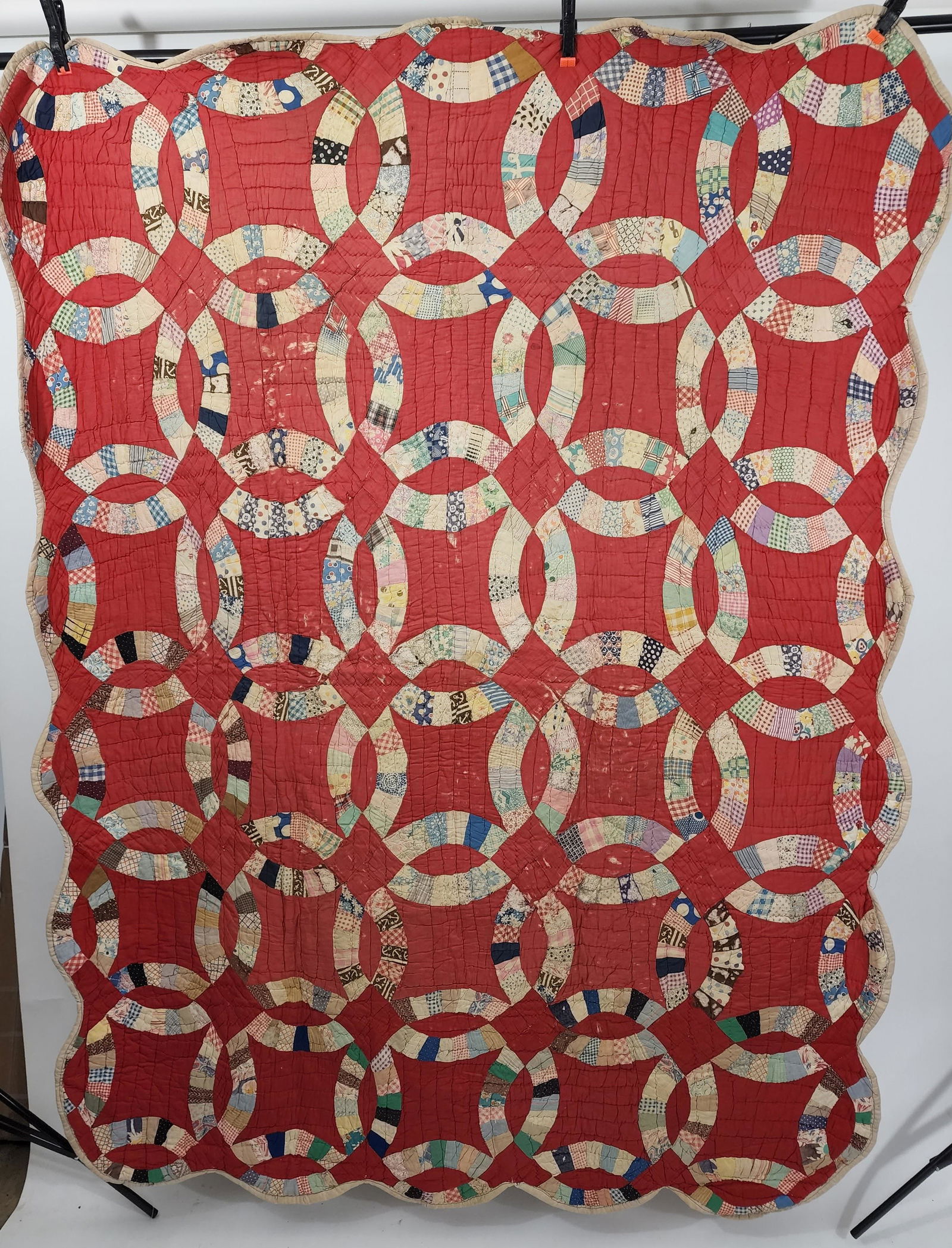 AMERICAN PIECED QUILT: 2nd quarter-20th century. Double Wedding Ring with red ground. Large format rings in polychrome cotton. Hand and machine done. Scallops on edges echo the rings. Thick batting, sparsely quilted using a