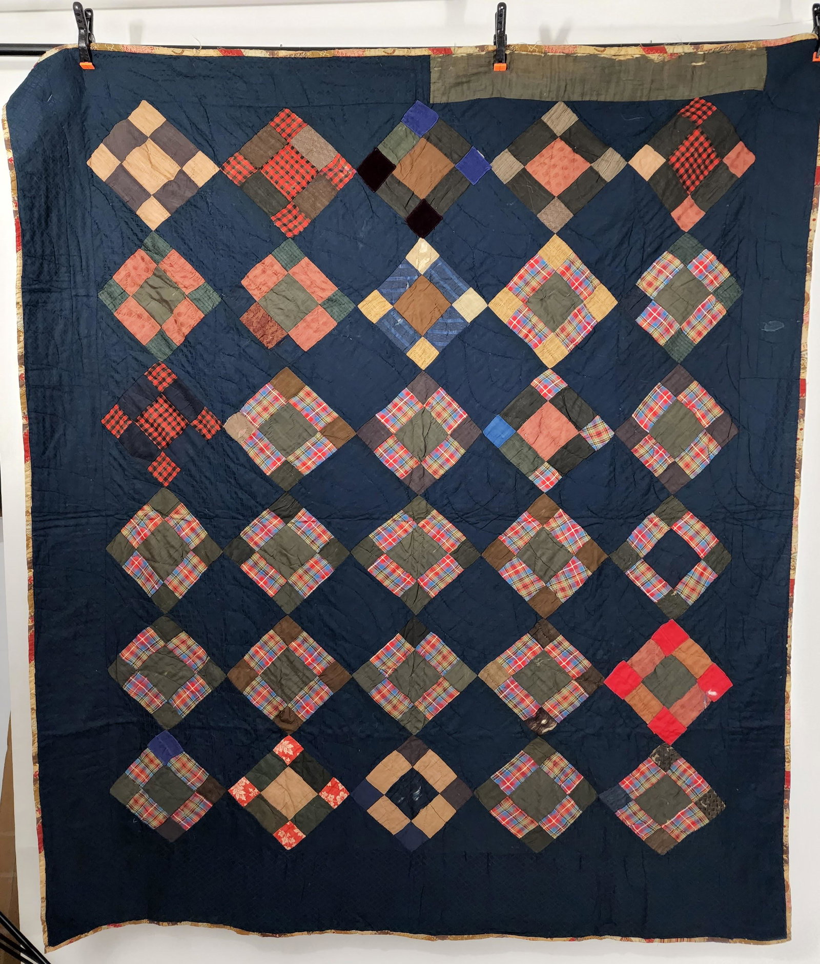 AMERICAN PIECED QUILT: C. 1900. Uneven nine patch on point with alternating blocks of figured navy blue fabric. Nine patch has many red and blue plaids and solid greens as well as other colors from that palate. Backing is a