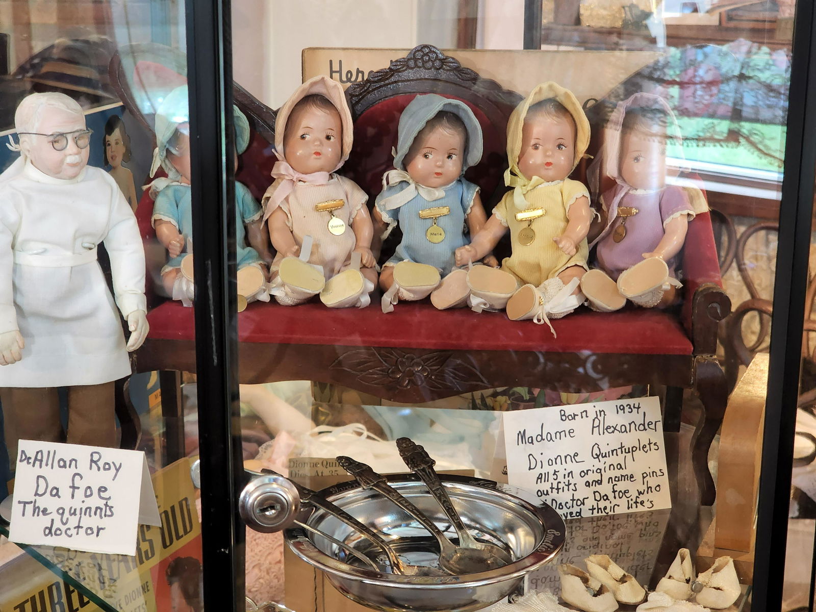 COLLECTION OF DIONNE QUINTUPLET MEMORABILIA AND MERCHANDISE: Collection includes books, various dolls, including Madame Alexander, table lamp, photos, hand fans, doll swing, baby dish with four spoons, and assorted collectibles and publicity material. Display c