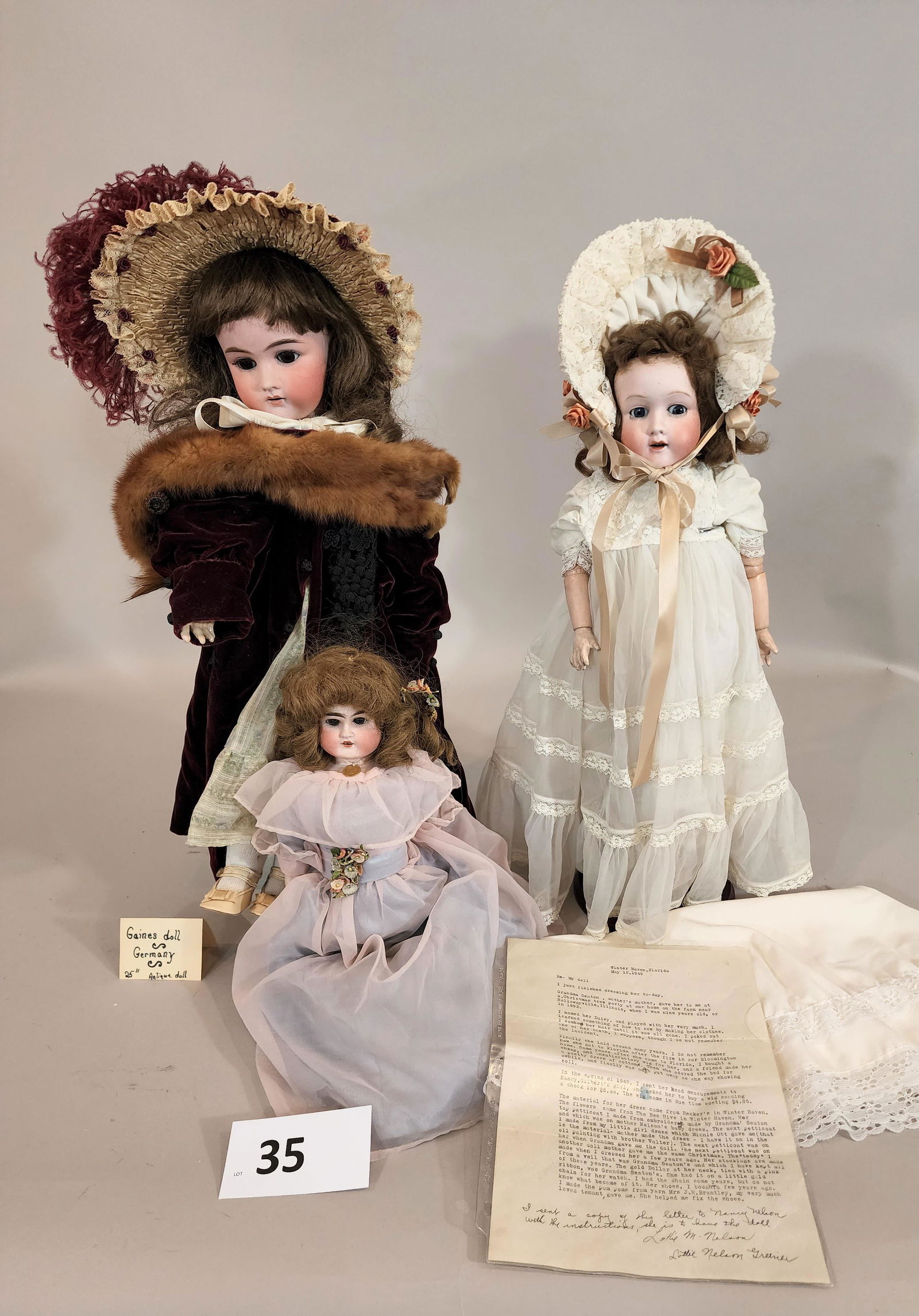 THREE BISQUE-HEAD DOLLS: All with composition bodies, one marked, the largest with a deep red velvet outfit and a mink stole, and the smallest with history. Largest is 23".