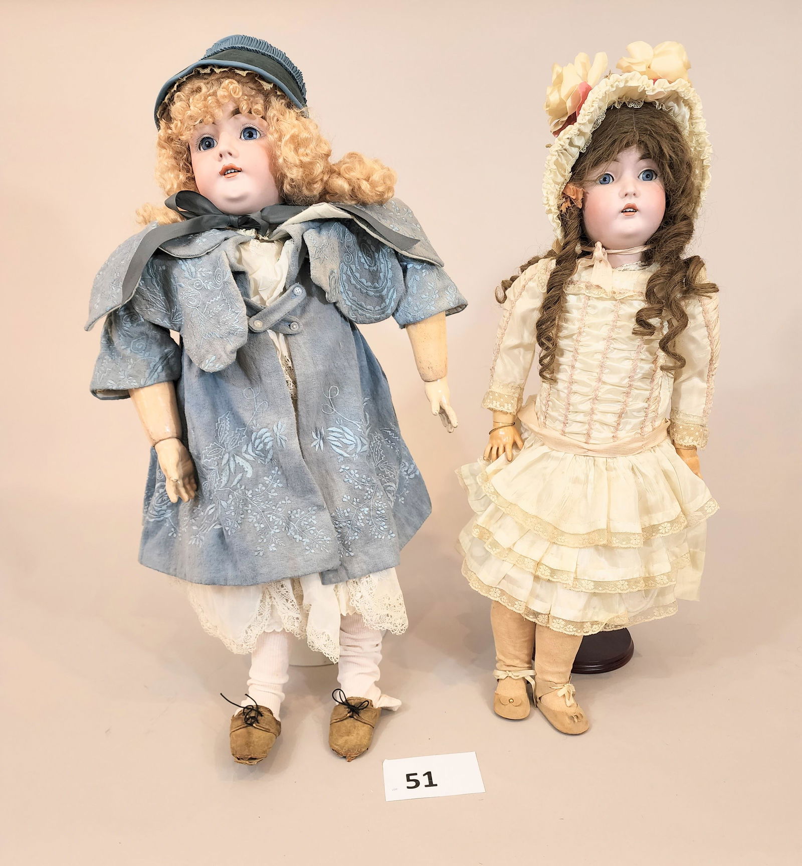 TWO KESTNER DOLLS: One blonde, one brunette, both bisque heads and composition bodies. Blonde in elaborate blue embroidered cloak, brunette in cream-colored silk and lace dress. 30" and 28" high.