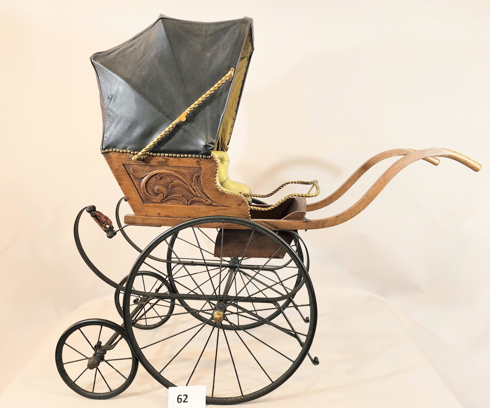 ENGLISH BABY CARRIAGE: Late 19th century, wood frame with pale green tufted leather upholstery and black leather canopy with silk lining. 52" long.