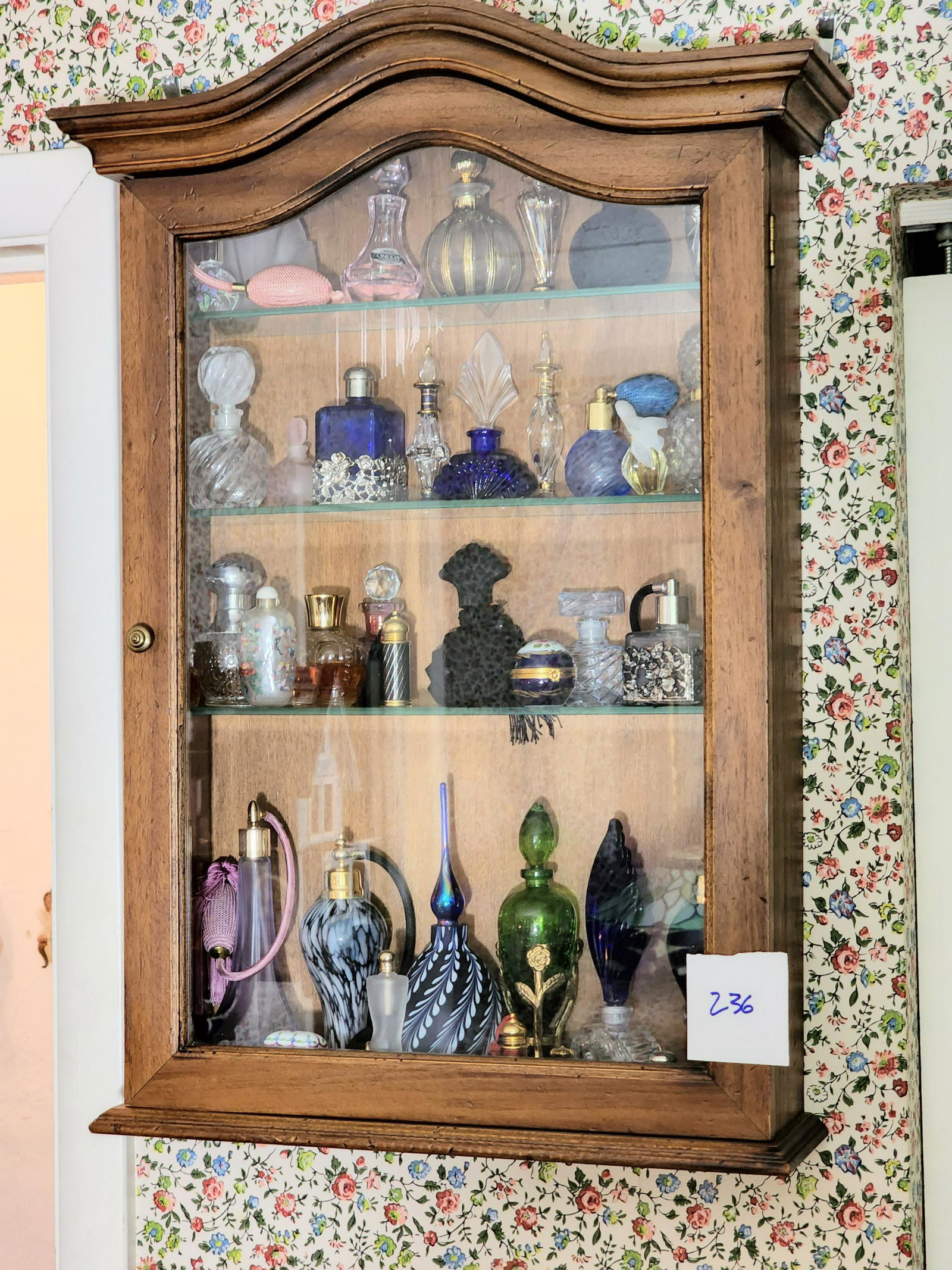 COLLECTION OF PERFUME BOTTLES: Mostly glass, some quite fancy, and sold in a walnut display case. Case is 28" high, 18" wide.