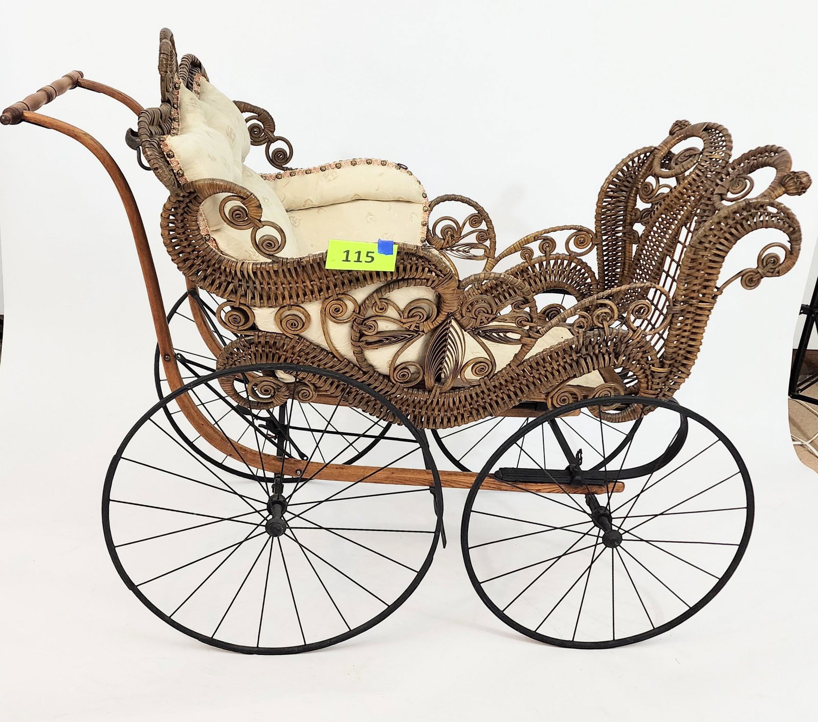 FANCY VICTORIAN BABY CARRIAGE: Ornate rattan work carriage with leaves, curlicues, and scrolls. Replaced ivory brocade upholstery. 50" long.