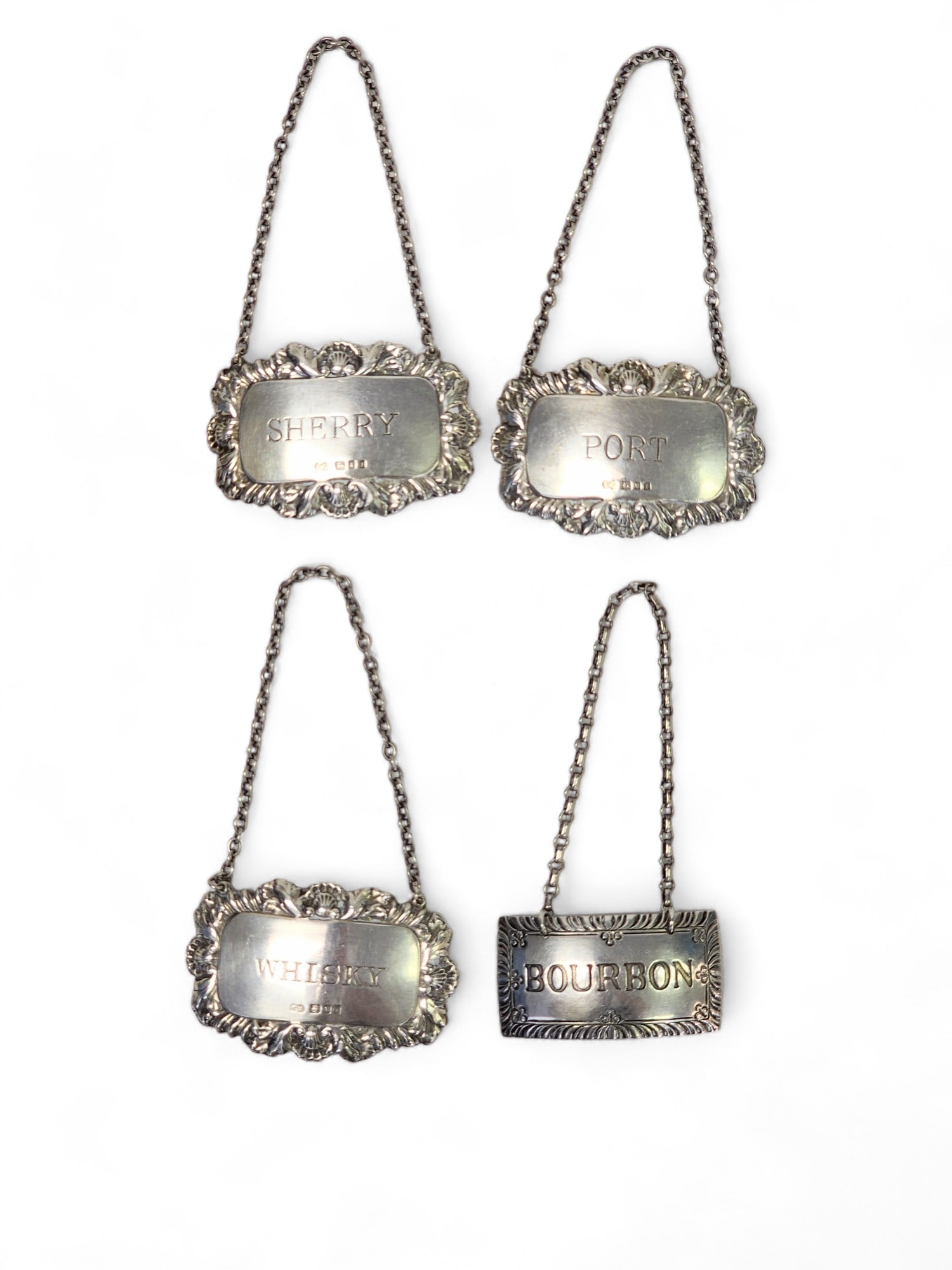 FOUR STERLING SILVER BOTTLE TAGS: Port, whiskey, and sherry are marked for London, 1964, and maker "NJ," and the bourbon tag is by Steiff. Total weight approx. 50g.