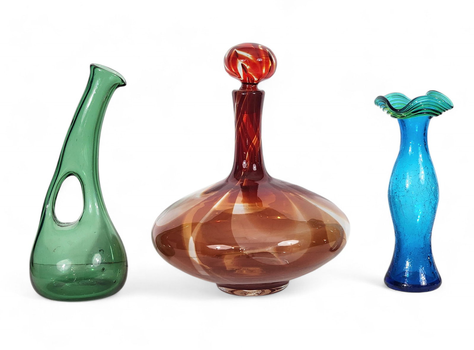 THREE PIECES OF MID-CENTURY GLASS: Includes a green pitcher (attr. to Empoli), 12.75" high, and two pieces of Blenko: a red Charisma decanter with swirled stopper, 13.25" high, and a blue and green crackle vase, 10.5" high.