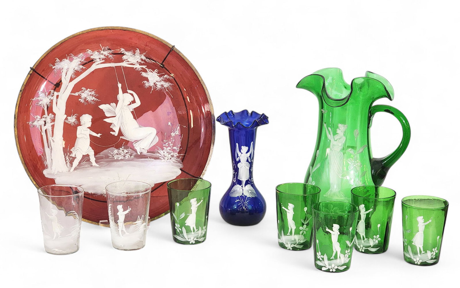 GROUP OF "MARY GREGORY" GLASSWARE: Late 19th century. White-enameled scenes (mostly children) on colored glass. Includes a green water set (pitcher and tumblers), cobalt vase, colorless tumblers, and a large ruby red charger. Charger i