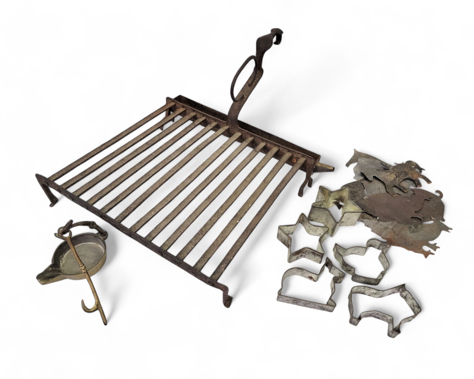 COLLECTION OF EARLY METALWARE: American, mid-late 19th century. Fire trivet with andiron feet and a strap handle with ring. 2.5"h. 12"w. 13"d. Five cookie cutters including stars and three animals. Brass grease lamp. 9"h. Eight she