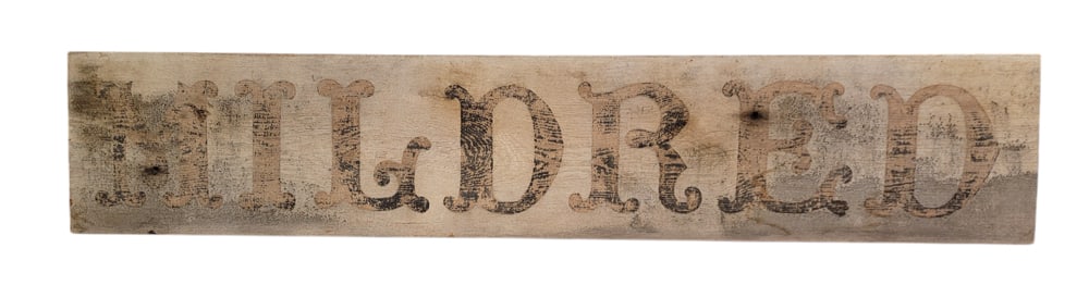 "MILDRED" SIGN: American, late 19th century, poplar. Original "MILDRED" in fancy font, and stenciled on the back "G.L. Randall.". 11.75" high, 60.25" long.