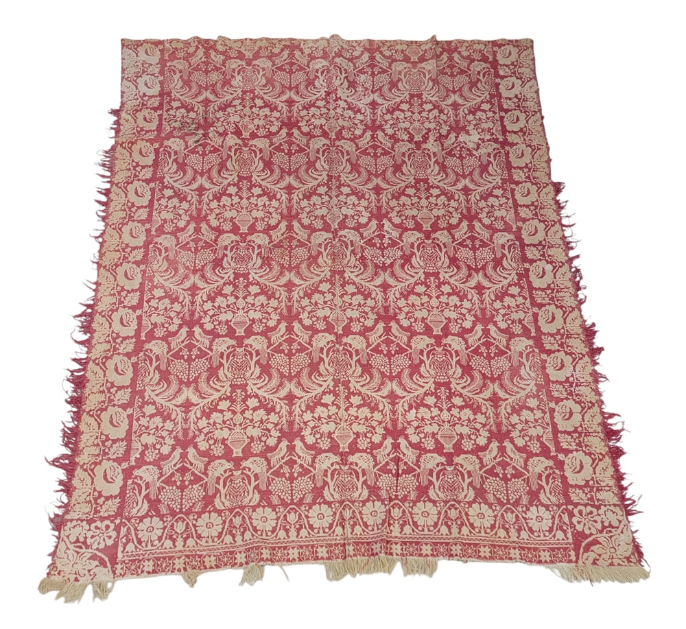 JACQUARD COVERLET: American, mid-19th century. A coverlet in pink with a centerfield of large floral urns and peacocks feeding their young, vine and rose side borders, floral and starburst foot borders, and floral corne