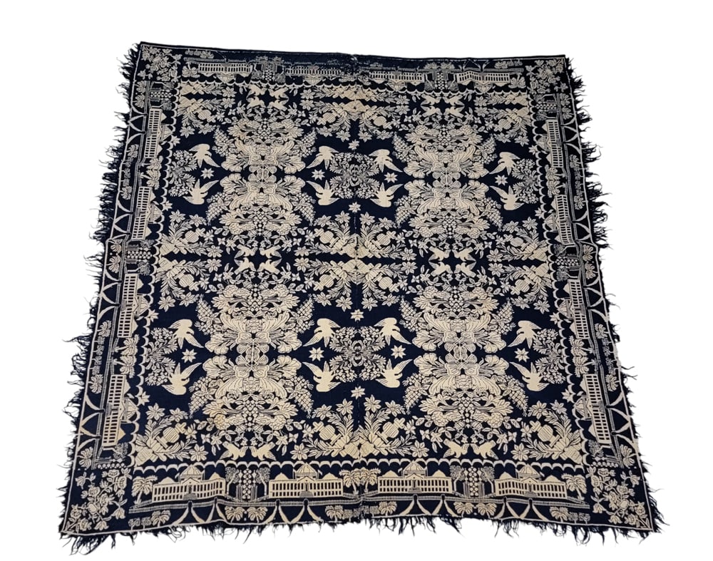 JACQUARD COVERLET: American, mid-19th century. A coverlet in dark blue with a centerfield of large floral medallions and eagles, Capitol building border with fence and palm trees, floral corner blocks. 79" by 70.5". Pro