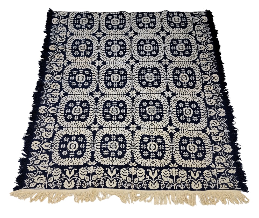 JACQUARD COVERLET: American, mid-19th century. A coverlet in dark blue with a centerfield of plumed floral medallions and offset eight-point stars, borders and corner blocks with tulips, flowers, and grapevines. 84" by 