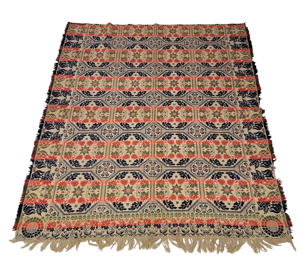 JACQUARD COVERLET: American, mid-19th century. A coverlet in dark blue, green, and red with a field of floral and foliate designs inset in octagonal shapes, floral side borders and a foliate foot border, corner blocks w